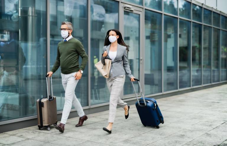 business travelers wearing face masks walk through an airport with luggage, representing the shift toward digital-first B2B buying and reduced reliance on in-person events