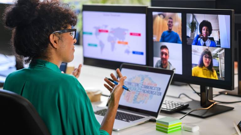 woman leading a webinar at her desk, viewing multiple remote participants on large monitors with a world map and data visuals, representing online workshops, live demos, and interactive learning events