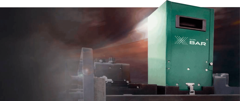 A green industrial machine labeled X BAR with a dark, industrial background and some metallic components partially visible. The lighting emphasizes the machine, creating a dramatic effect with shadows and highlights.