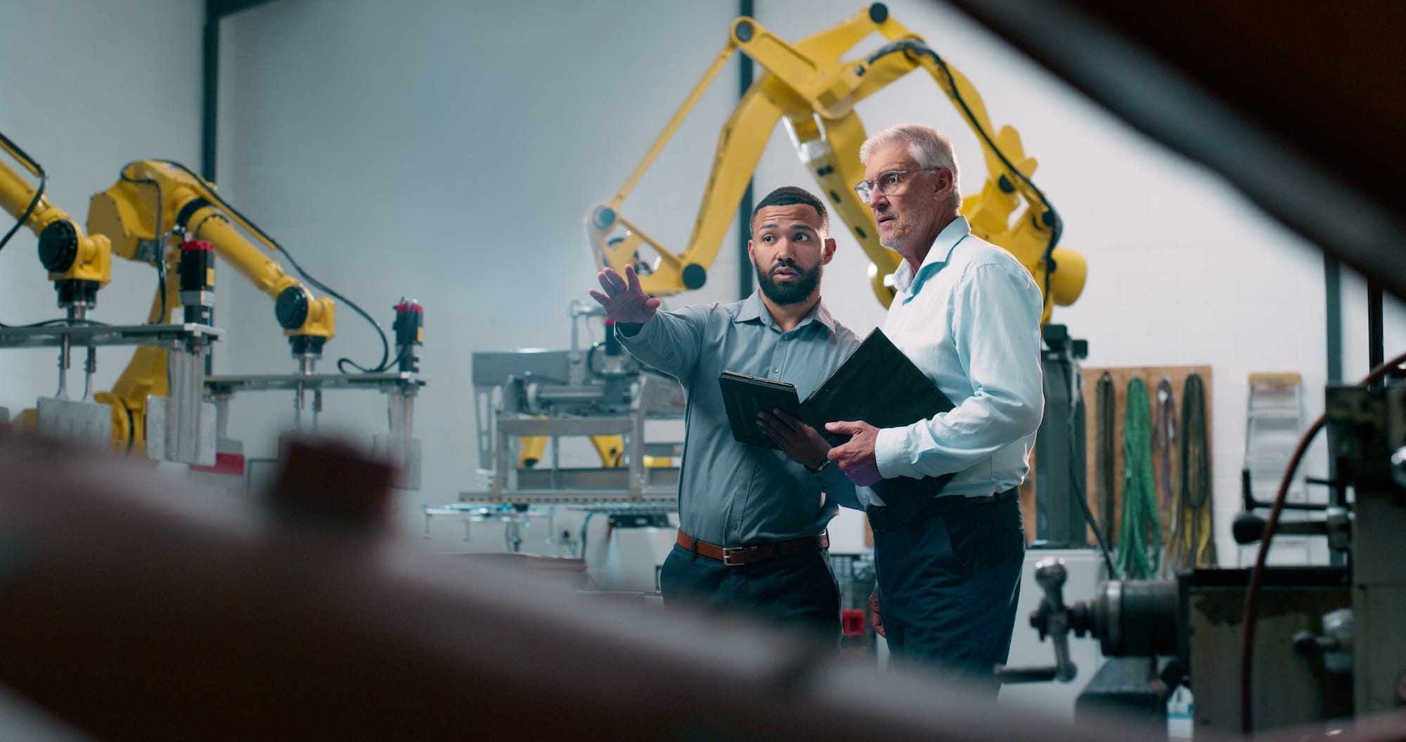 engineers review CNC production details on a tablet inside a modern automated facility, surrounded by robotic equipment. The scene reflects how today’s CNC buyers engineers and procurement teams expect fast access to specs, capabilities, and clear evaluation information